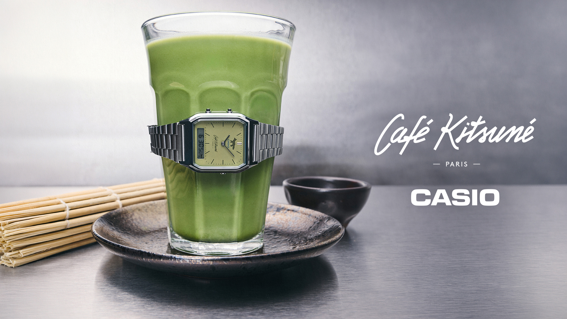 卡西欧(CASIO)与Café Kitsuné联名腕表AQ-230ECK-3A的主视觉图,表带缠绕在一杯抹茶饮品上
